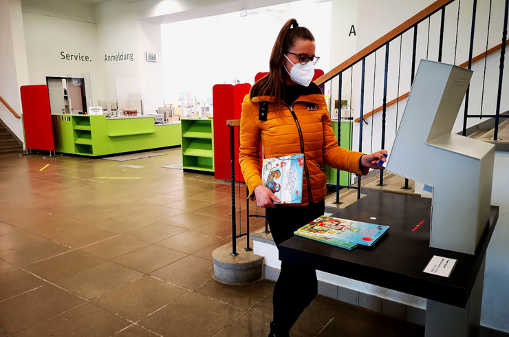 Eine Person mit Maske am Selbstverbucherautomat im Eingangsbereich der Stadtbibliothek