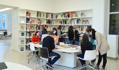Eine Gruppe von Menschen in einer Bücherei an einem Tisch und den Bücherregalen.