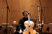 Ein junger Musiker sitzt mit seinem Violoncello in einem Konzertraum