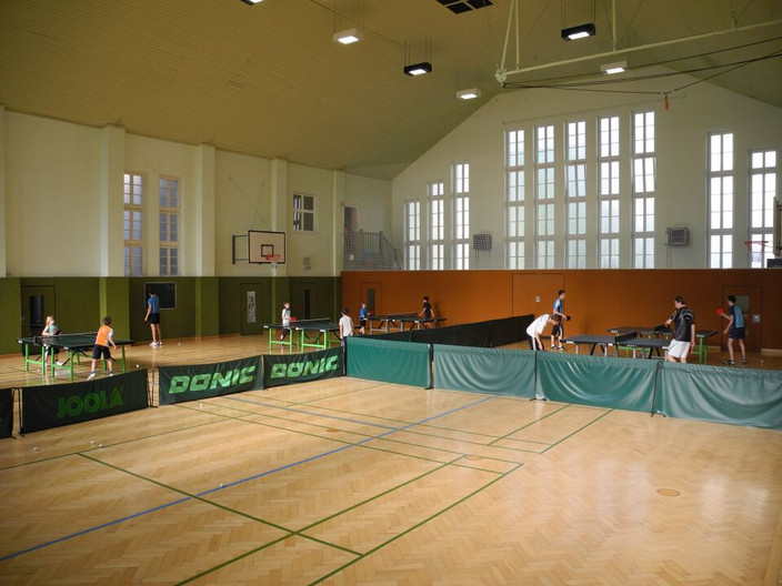 Sporthalle Breitschuhstraße in der mehrere Kinder und Jugendliche Tischtennis an mehreren Tischen spielen.