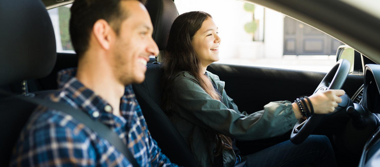 Glückliches Mädchen fährt Auto, ihr Vater sitzt daneben. 