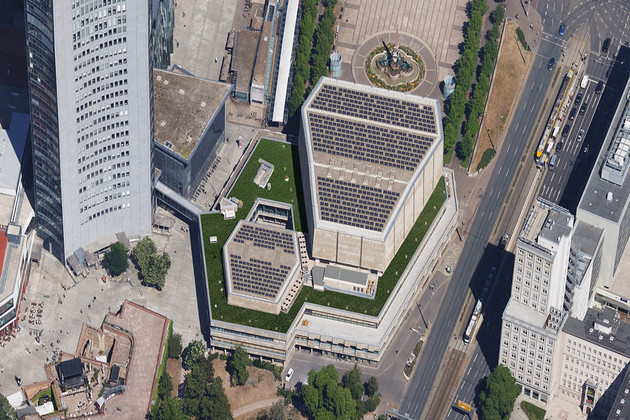 Vogelperspektive auf ein Dach mit Dutzenden Photovoltaikmodulen umrahmt von einer grünen Fläche.