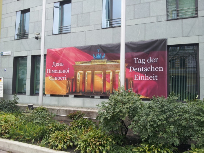 Ankündigung des Tages der deutschen Einheit am grauen Gebäude der deutschen Botschaft in Kyjiw mit einem großen roten Werbeschild