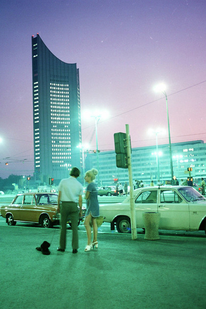 Das City-Hochhaus 1973 in der Abenddämmerung. Zwei Menschen stehen neben der Straße an der zwei Autos geparkt sind.