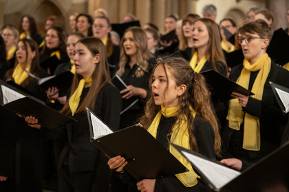 Mädchenchor in Schwarz mit gelbem Schal und Liedheften
