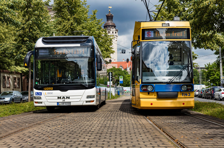Ein Bus und eine Straßenbahn der Leipziger Verkehrsbetriebe stehen nebeneinander. Im Hintergrund ist der Turm des Neuen Rathauses sichtbar.