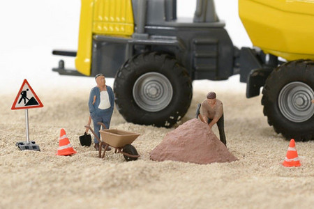 Baustellenszene mit Spielfiguren und Spielzeuglaster im Sand