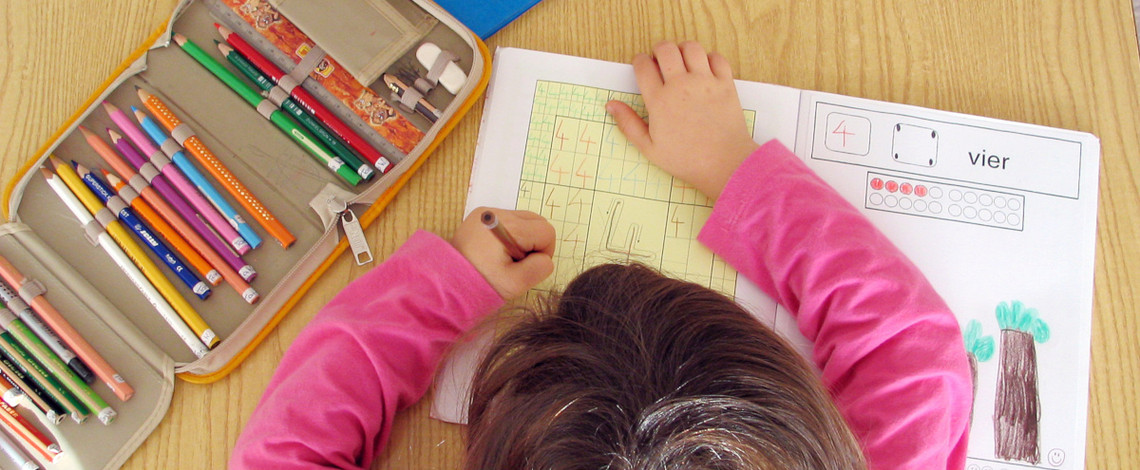 Mädchen schreibt mit der linken Hand in ein Aufgabenblatt