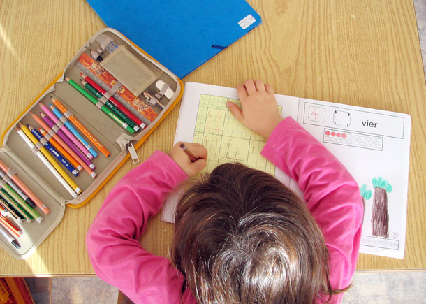 Mädchen schreibt mit der linken Hand in ein Aufgabenblatt