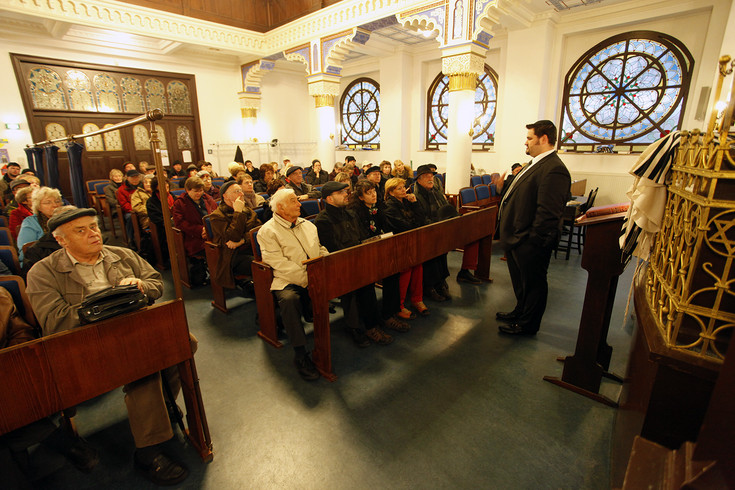 Der Rabbiner Zsolt Balla steht in einer Synagoge vor vollbesetzten Sitzreihen.