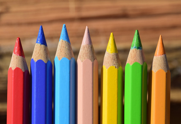 Man sieht sieben Buntstifte in verschiedenen Farben in einer Reihe.