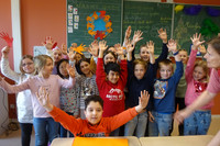 Viele Kinder stehen vor einer Tafel und halten die Hände nach oben