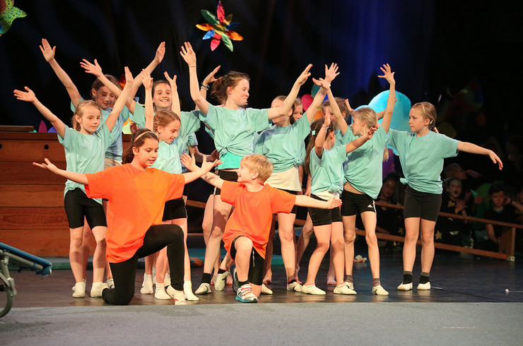 Ein Dutzend Kinder in grünen und zwei in orangefarbenen Shirts zeigen eine Choreografie auf der Bühne