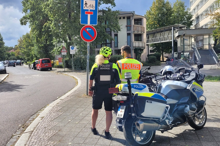 Rückenansicht von Ordnungsamt-Bedienster und Polizist mit Motorrad und Fahrrad neben einem Parkverbotschild