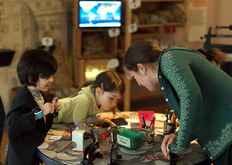 Zwei Kinder und eine Frau schauen auf einen Tisch mit Bastelmaterial im Kindermuseum Leipzig.