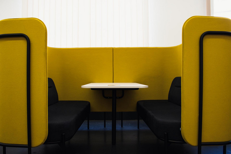 Eine gelbe halbrunde Eckcouch mit Sichtschutz und einem Tisch