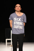 Ein Mann steht stark geschminkt auf der Bühne. Er trägt ein T-Shirt mit der Aufschrift "Six String Guitar"