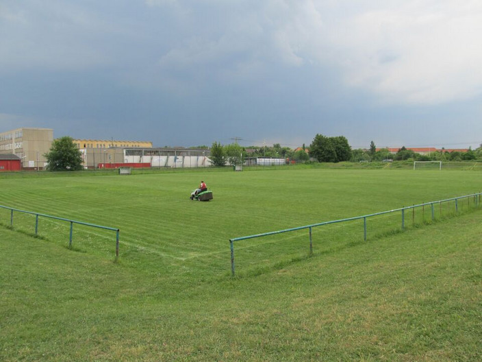 Großes Fußballrasenfeld der Kurt-Kresse-Kampfbahn. Ein Mann mäht mit einem kleinen Traktor Rasen.