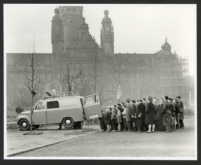 Schwarz-weiß Foto von Menschen die vor einem Auto stehen.