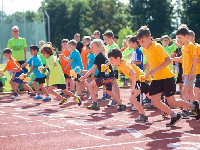Kinder in orangenen T-Shirts bei einem Staffellauf im Sommer
