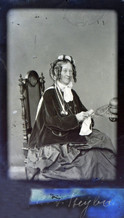 Porträtfoto einer Frau mit kunstvoller Frisur und Brille im Lehnstuhl sitzend und Handarbeiten anfertigend