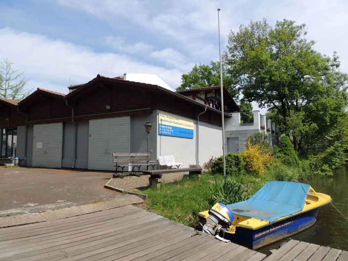 Bootshaus der Wassersportanlage Ziegeleiweg mit einem abgedeckten Motorboot auf dem Wasser.