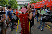 Straßenszene in einer chinesischen Stadt. Eine schwarzer Mensch umarmt einen Chinesen, der ein rotes Banner mit Schriftzeichen hält.