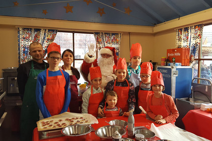 Der Weihnachtsmann posiert mit Kindern und Helfern in der Wichtelwerkstatt