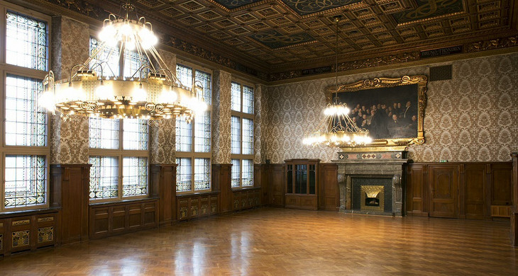 Blick in den leeren prachtvollen Ratsplenarsaal im Neuen Rathaus. Von der aufwendig gestalteten Decke hängen zwei Kronleuchter.