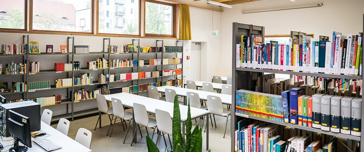 Moderne Schulbibliothek mit Bücherregalen und Computer sowie Tischen