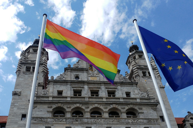 Die Regenbogen- und die Europafahne wehen nebeneinander, im Hintergrund das neue Rathaus.