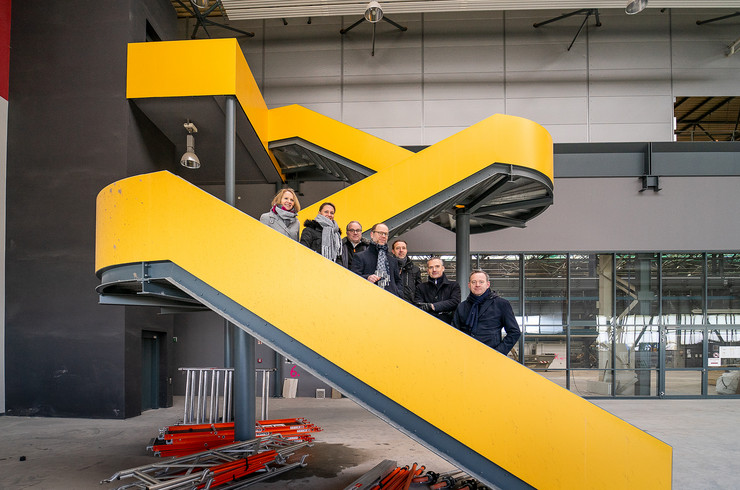 Zu sehen ist eine gelbe Treppe in einer großen leeren Produktionshalle, auf der Treppe stehen aufgereiht von links nach rechts: Andrea Bulla (MIB AG), Anne Langhof (SENEC GmbH), Thomas Augat-Kaiser (SENEC GmbH), Clemens Schülke (Wirtschaftsbürgermeister Stadt Leipzig), Sascha Stabenow (MIB AG), Dr. Alexander Schlag (MIB AG), Maik Mehlhose (MIB AG) in der Produktionshalle des neuen Unternehmenshauptsitzes von SENEC