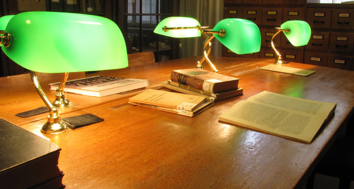 Die Lese- und Arbeitsplätze der Bibliothek der Leipziger Schulmuseums. Zwei gegeneinander gestellte Tische, vier Leselampen mit grünen Glasschirmen, zudem Literatur. .
