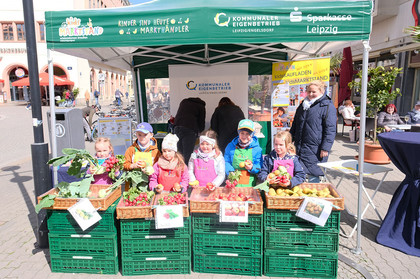 Sechs Kinder stehen hiner grünen Kisten und halten Obst und Gemüse in den Händen. 