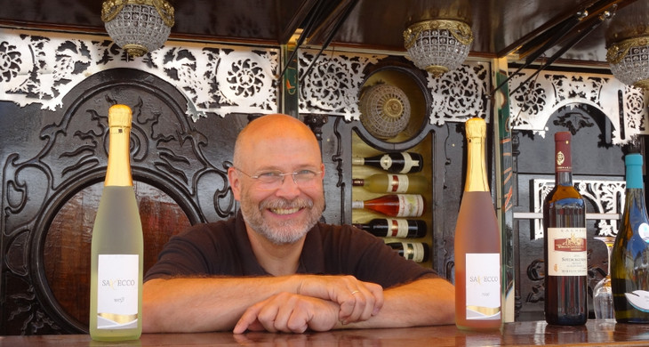 Mann lacht zwischen zwei Weinflaschen hindurch