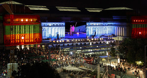 Zuschauer bei Nacht vor dem Hauptbahnhof Leipzig. An die Fassade sind Lichter und Videos projiziert.