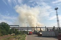 Eine Rauchwolke über einem Betriebsgelände eine Recyclinganlage. Feuerwehrautos löschen den Brand.