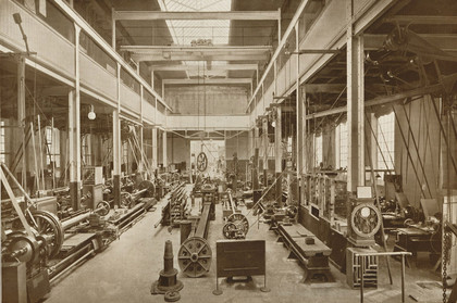 Sepia-Aufnahme einer Industriehalle zu Beginn des 20. Jahrhunderts mit vielen riemngetriebenen Drehbänken links und rechts aufgereiht