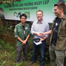 Drei Herren, zwei mit Handschlag, posieren für ein Foto vor dem grün-weißen Logo des Centers, umgeben von grünen Pflanzen