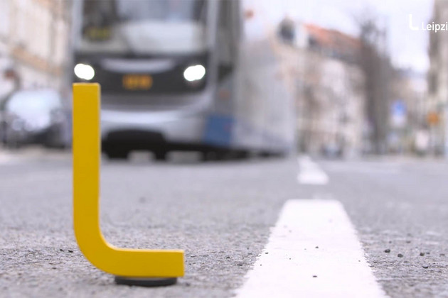 Ein gelbes L steht auf einer Straße, dahinter kommt eine Straßenbahn angefahren. 
