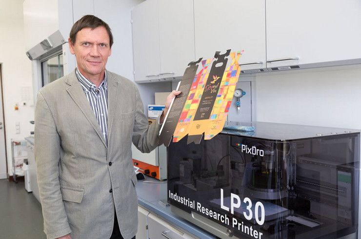 Prof. Eugen Herzau an einer für Forschungszwecke optimierten Digitaldruckmaschine. In der Hand hält er einen digital bedruckten Weinkarton.