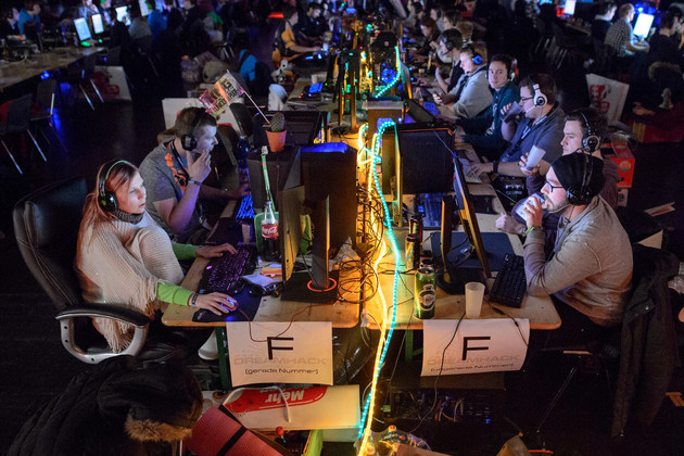 In einem dunklen Raum sitzen viele Computerspieler an ihren Rechner. Es sind zwei Reihen von Spielern, die sich gegenübersitzen.