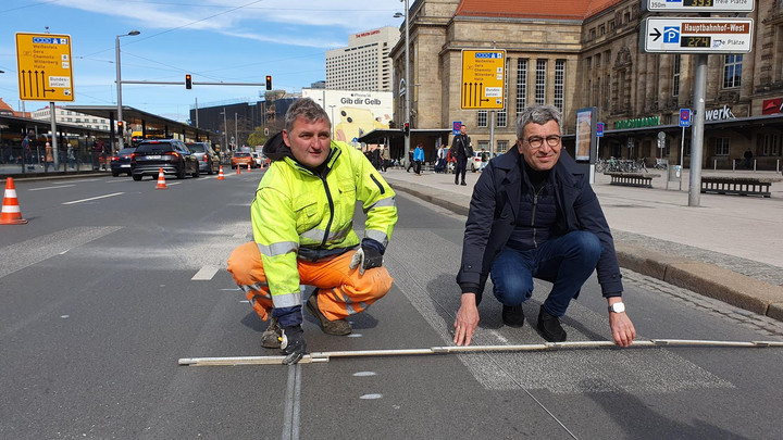 Zwei Männer mit Warnweste messen mit dem Zollstock auf der Straße neben dem Fußweg am Hauptbahhof.