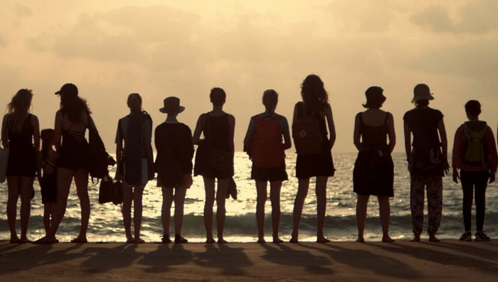 Eine Gruppe junger Menschen schaut auf das Meer bei untergehender Sonne