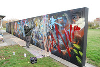Ein Mann besprüht eine bunte Graffitiwand.