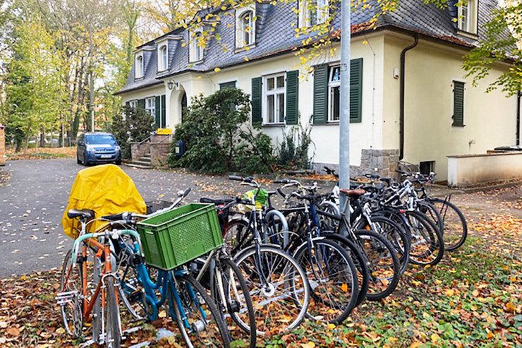 Mehrere Fahrräder stehen aufgereiht in einem Park vor einem Haus.