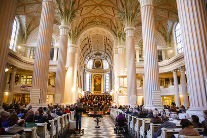 Innenraum der Nikolaikirche mit hohen Säulen und vielen Besuchern, im Altaraum ist ein Chor.