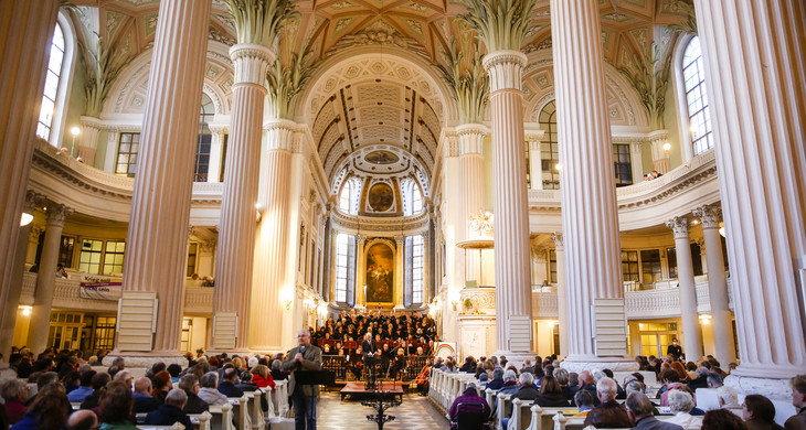 Innenraum der Nikolaikirche mit hohen Säulen und vielen Besuchern, im Altaraum ist ein Chor.