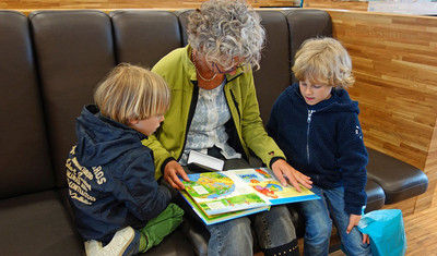 Eine ältere Dame liest zwei Kindern ein Buch vor.
