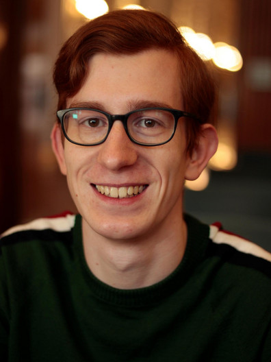 Quentin Kügler - Ein junger Herr mit Seitenscheitel und Brille lächelt ins Bild